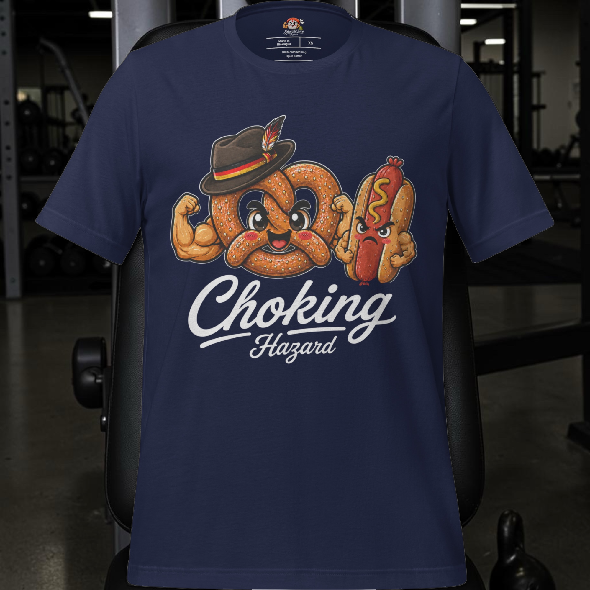 Introducing the Choking Hazard Tee - Germany Edition by Straight Face Originals—a navy blue Bella + Canvas 3001 t-shirt showcasing a cartoon pretzel and hot dog, both with smiling faces, flexing their muscles. The playful text “Choking Hazard” beneath the design gives this German Pretzel tee a witty edge, making it an ideal choice for anyone wanting a standout dating profile warning shirt. Displayed on gym equipment for added humor, it’s perfect for those who appreciate unique and clever apparel.